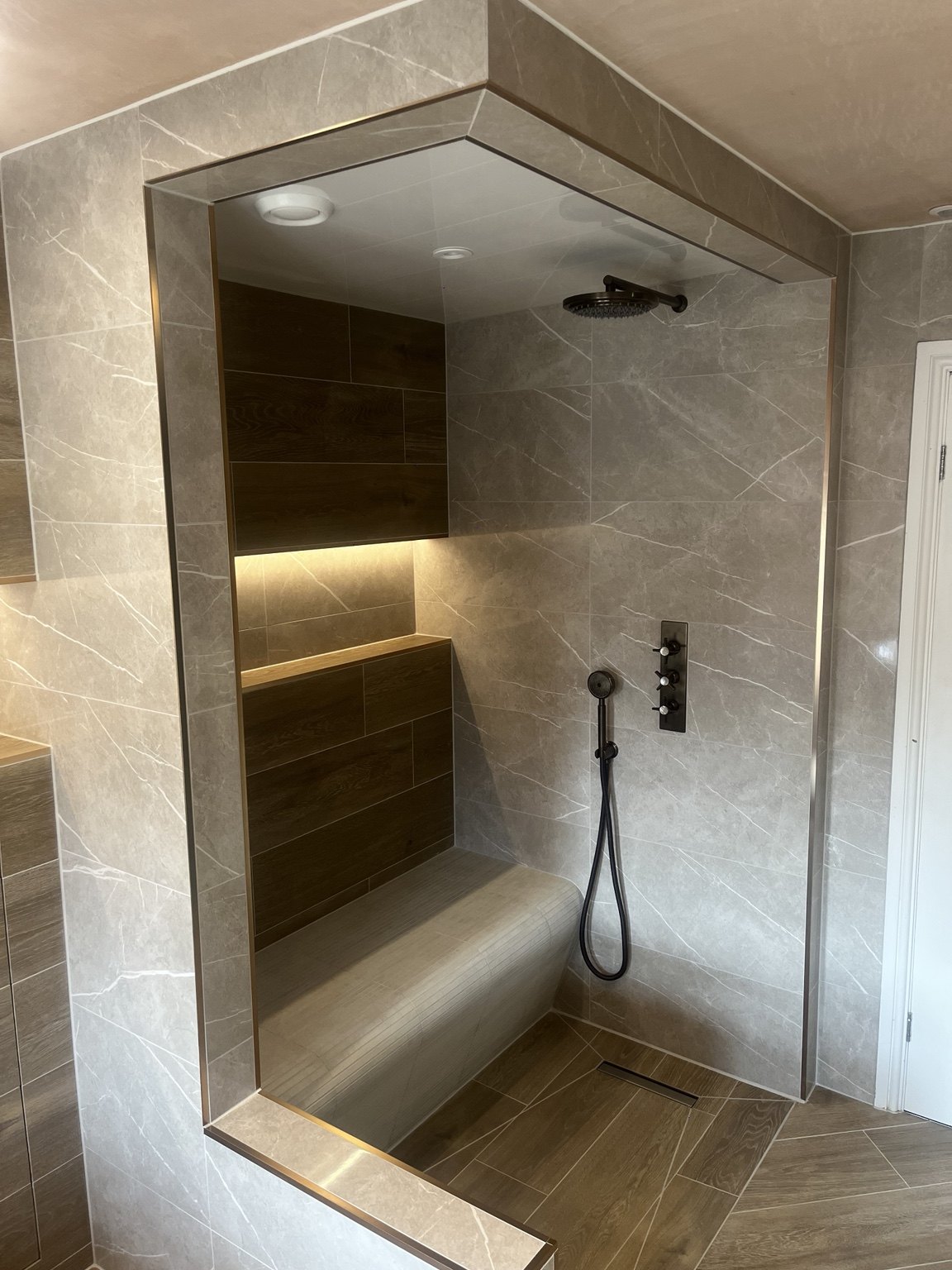 SG tiled shower with a built-in bench, wood-effect feature wall and illuminated niche