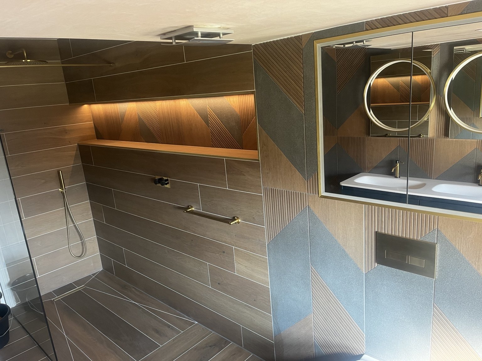 Wood-effect shower tiling, geometric feature wall and a long illuminated niche