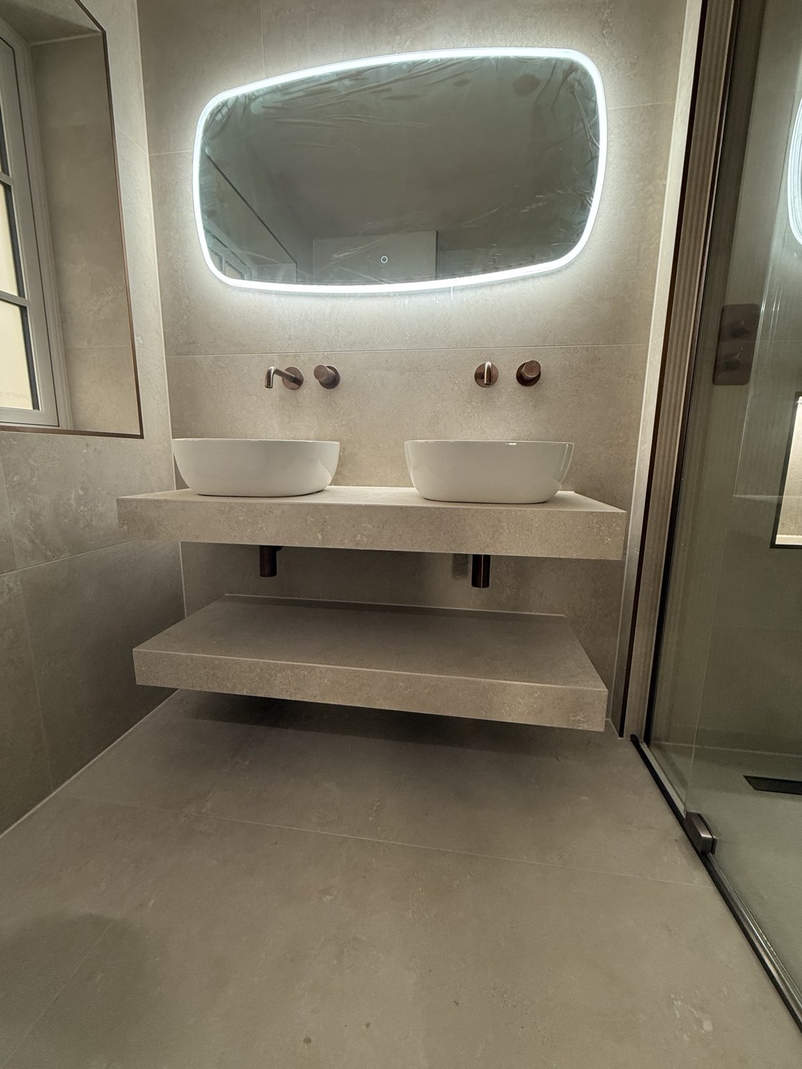 Twin countertop basins on floating tiled shelves beneath an illuminated mirror